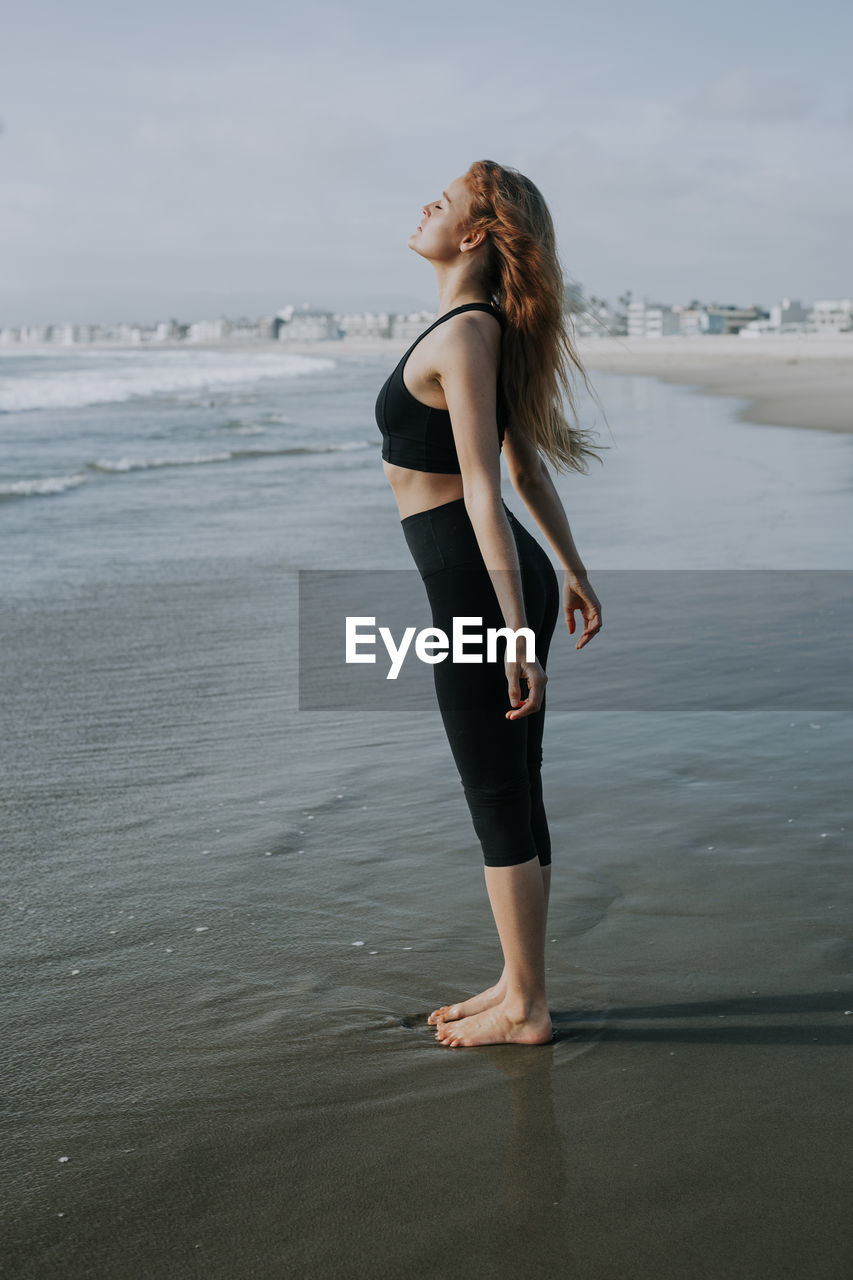 Young woman standing with eyes closed on shore at beach