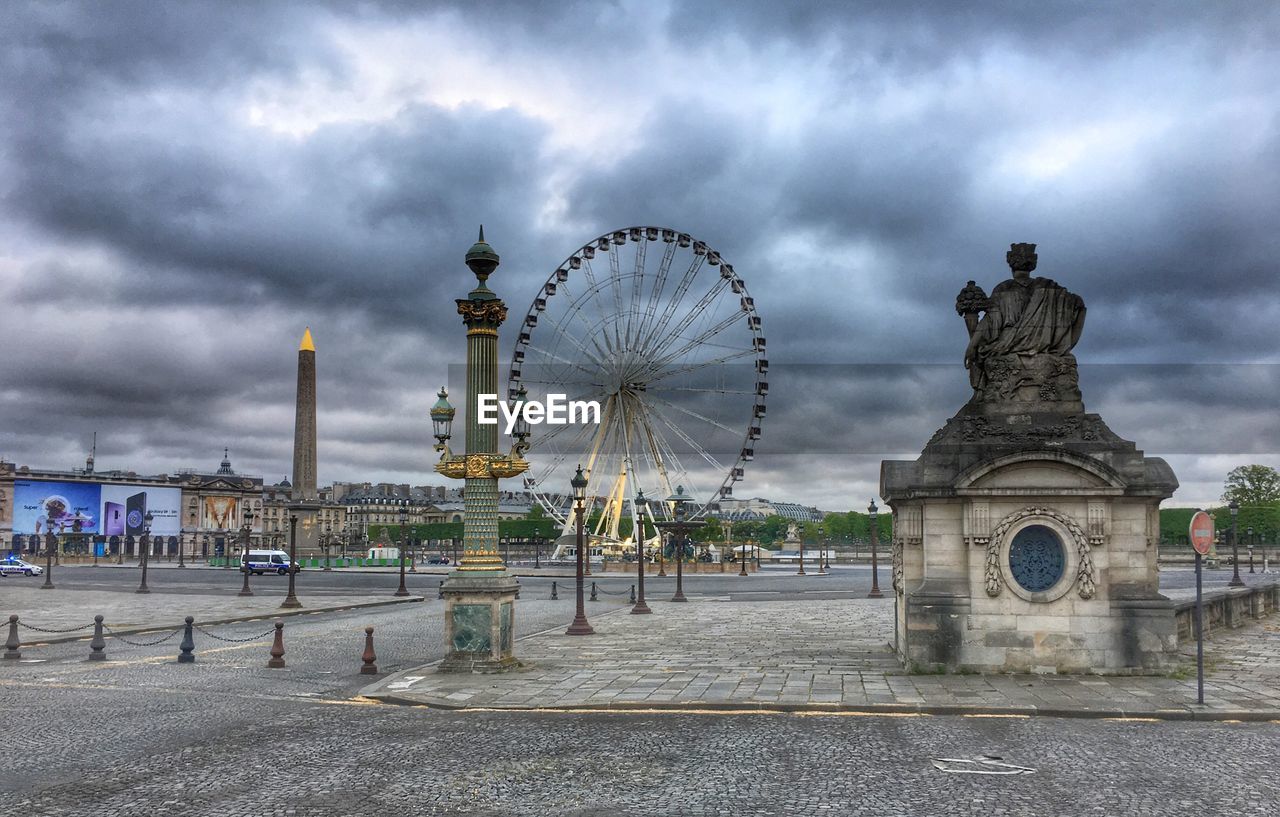 Ferris wheel in city against cloudy sky