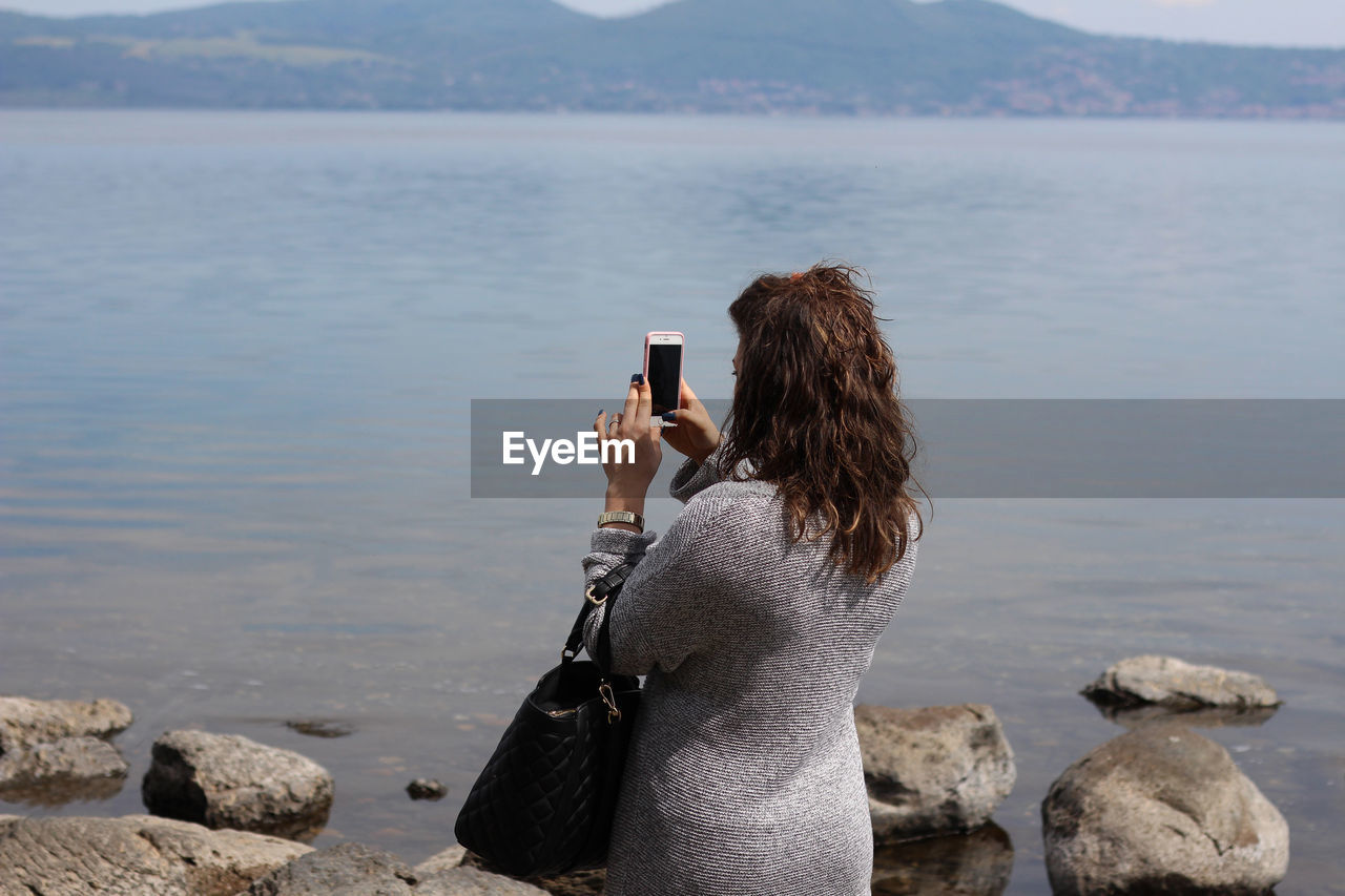 Rear view of woman photographing with mobile phone at beach