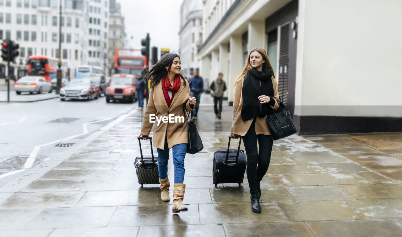 Uk, london, two friends exploring the city, arriving with trolley bags