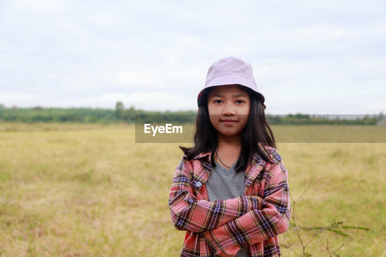 The little asian girl stands confidently with her arms crossed at the tropical farm field,