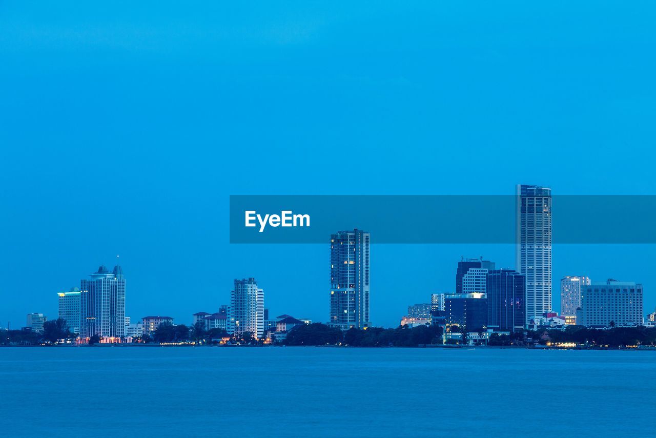 Sea by illuminated city against clear blue sky