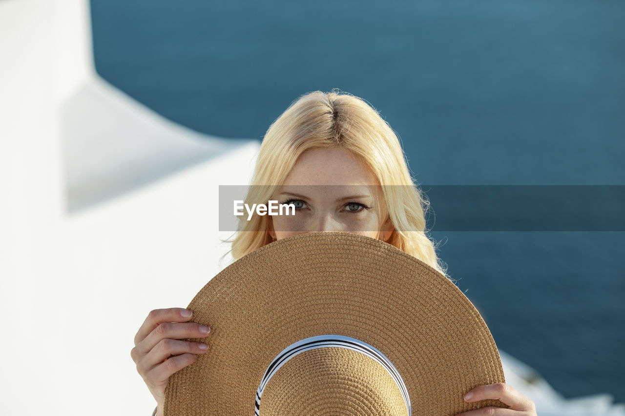 Portrait of beautiful woman holding hat in front of face