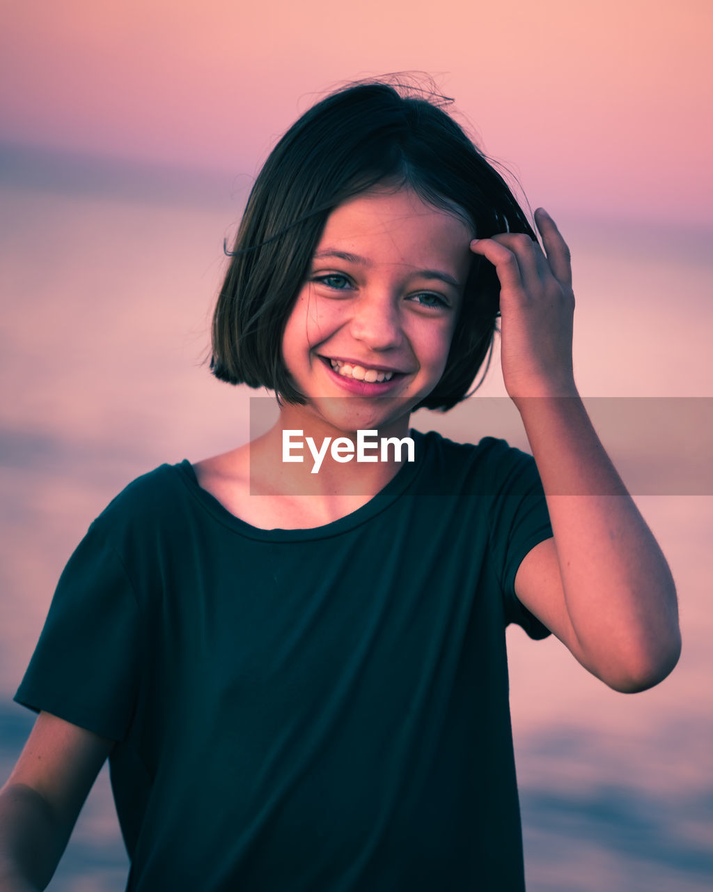 Close-up of smiling girl standing against sea during sunset