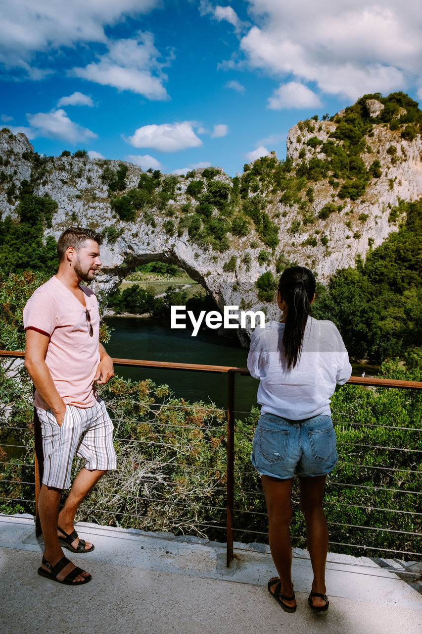 Couple standing by railing against mountain and sky