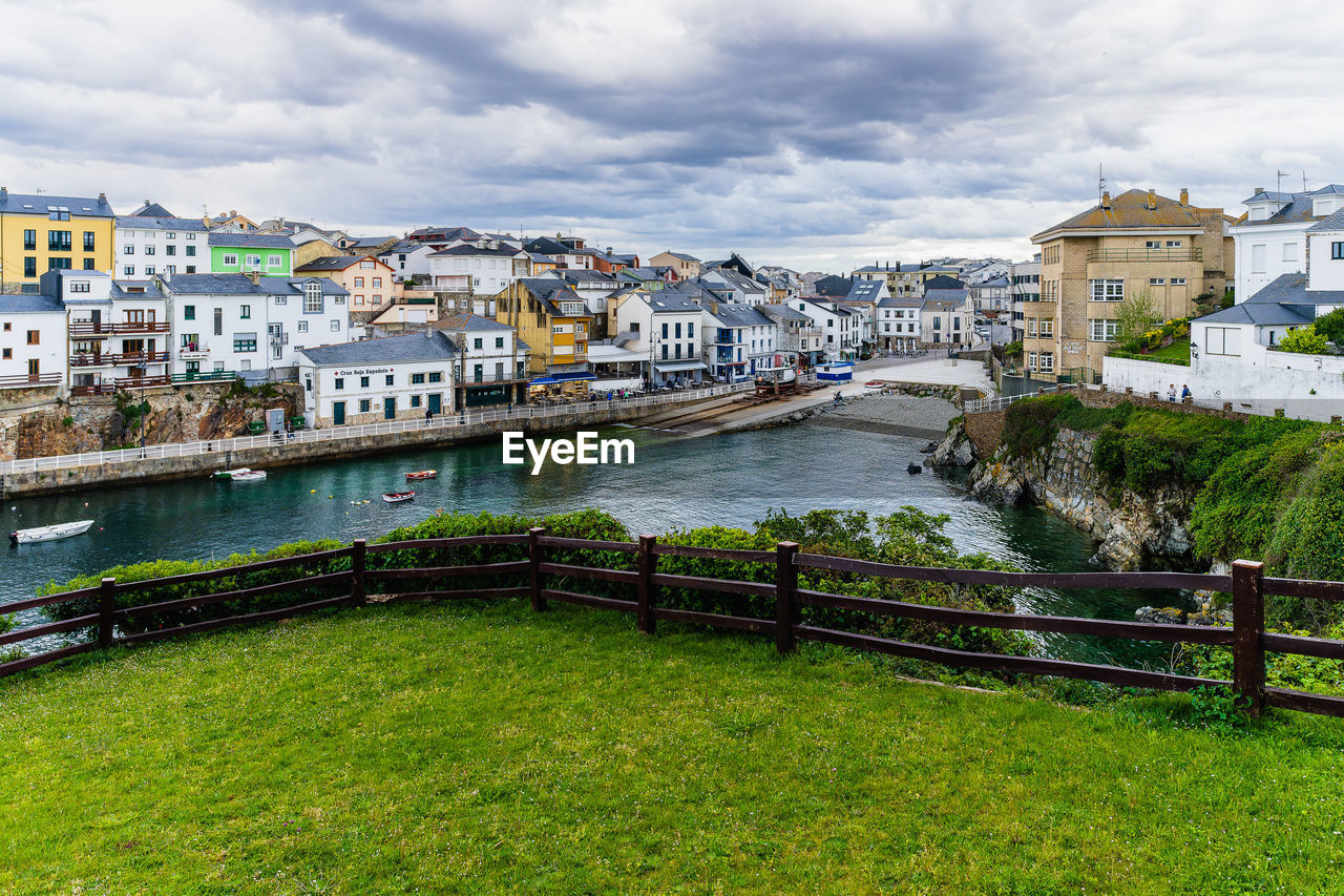 Buildings by river against cloudy sky