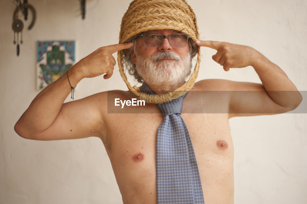 Portrait of shirtless man wearing basket on head while gesturing against wall