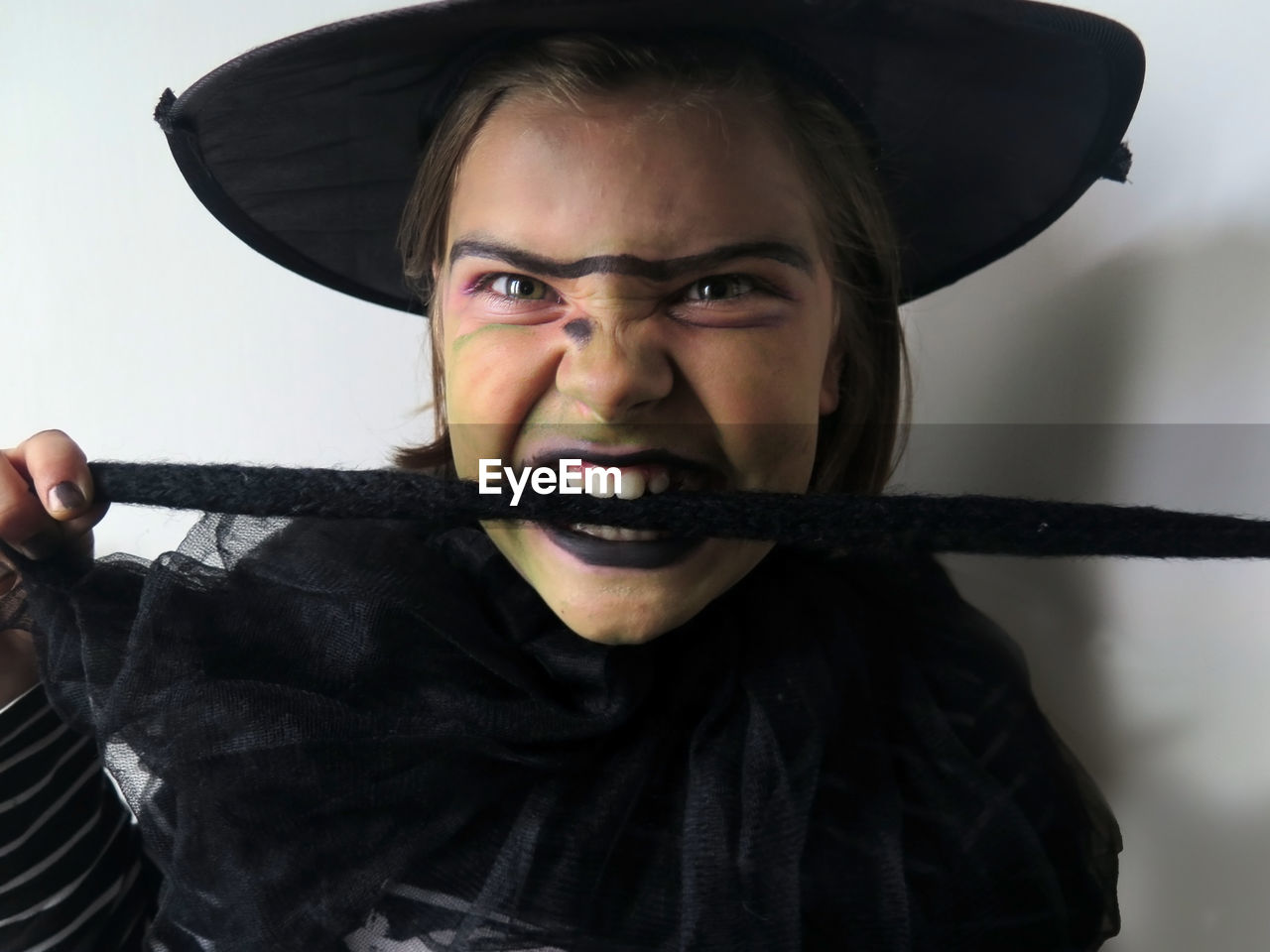 Portrait of girl wearing witch costume and hat biting cloth against wall at halloween