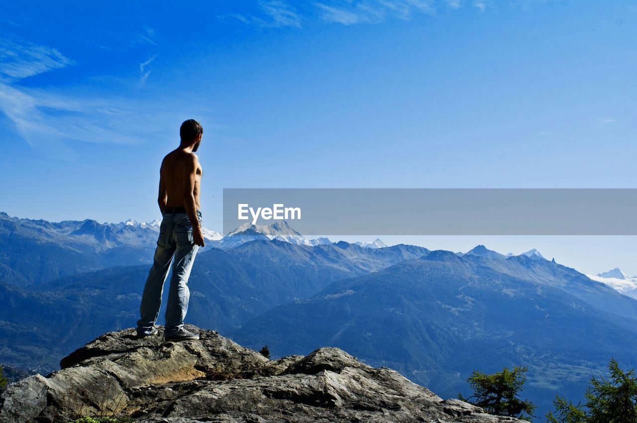 Rear view of shirtless man standing on mountain against sky