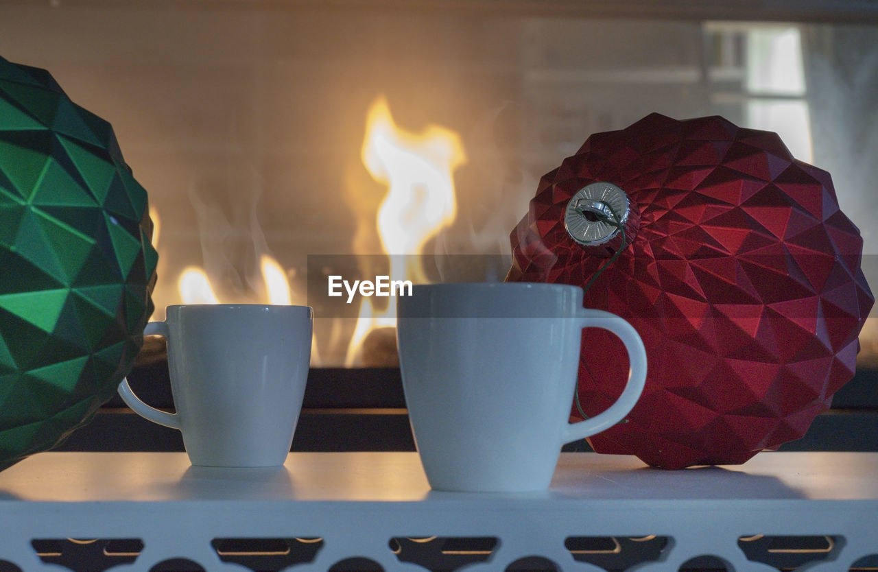 Close-up of coffee cups and decoration on table against fireplace at home