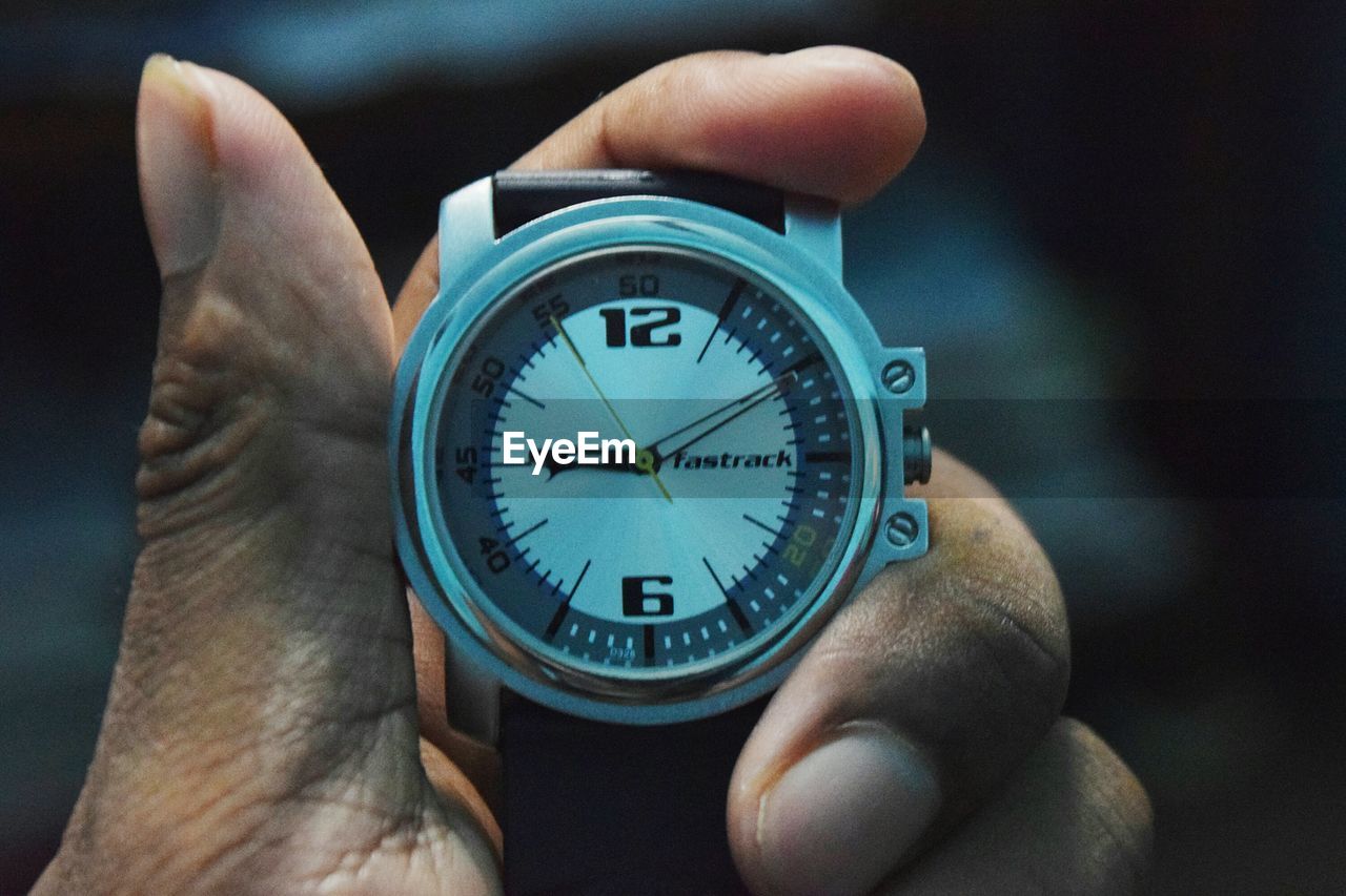 CLOSE-UP OF HAND HOLDING CLOCK AGAINST BLURRED BACKGROUND