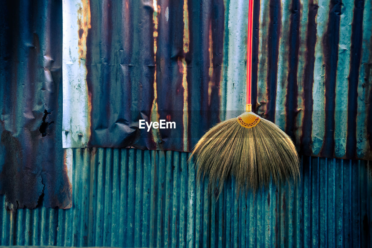 Broom hanging by rusty metal fence