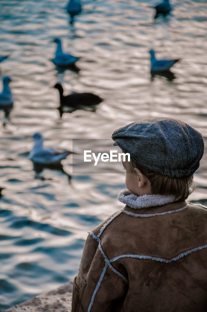 Boy in warm clothing looking at birds swimming in lake
