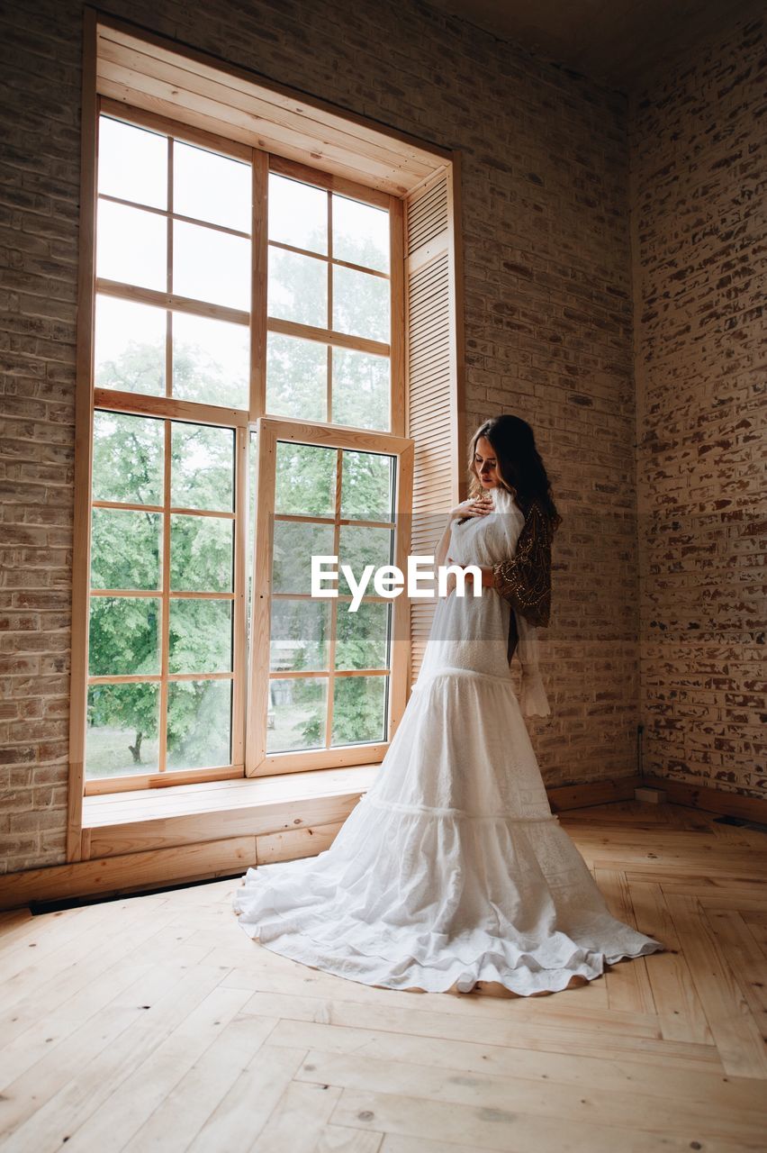 Woman holding wedding dress while standing against wall