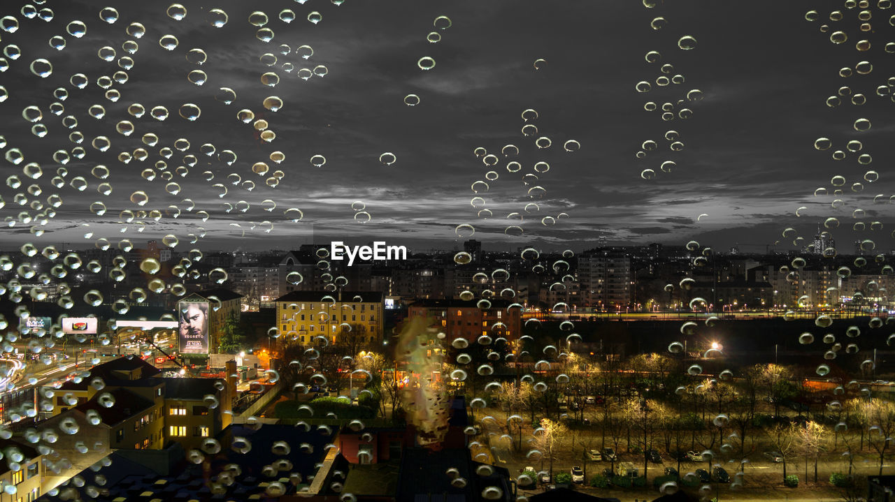 CLOSE-UP OF WET ILLUMINATED CITY AGAINST SKY AT NIGHT