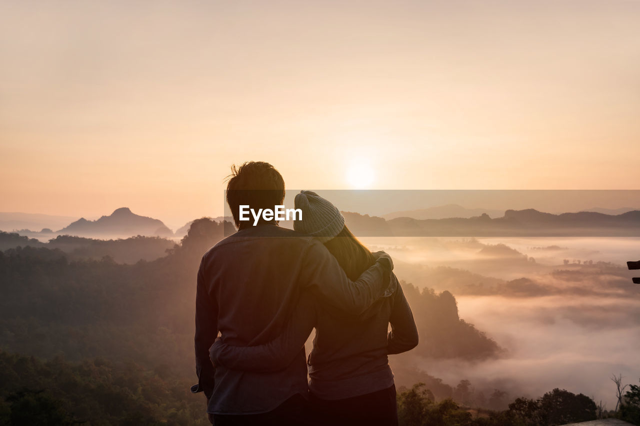 Rear view of couple standing against mountains during sunset