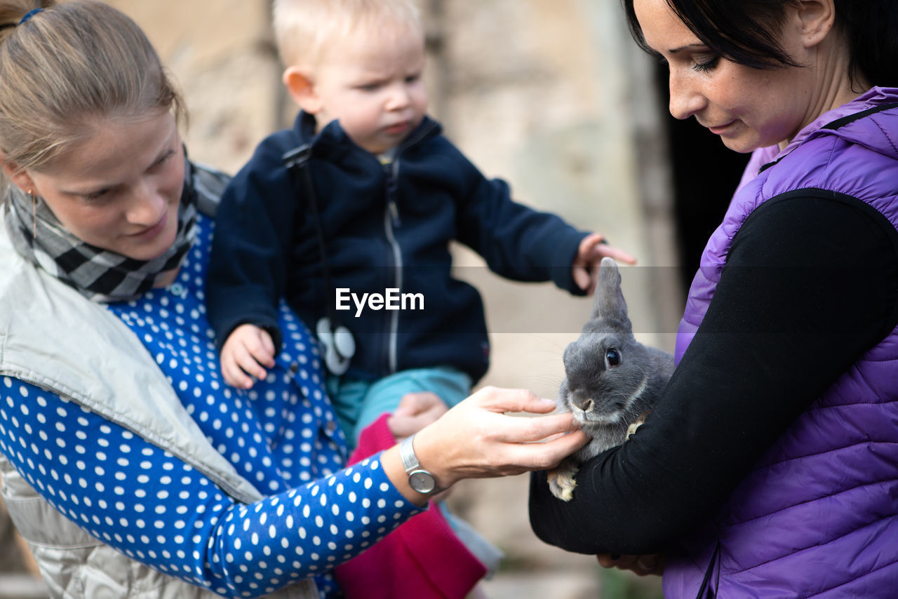 Mother with son looking at rabbit being held by woman in park