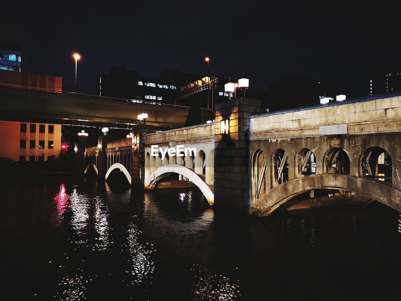 Illuminated bridge over river against sky in city at night