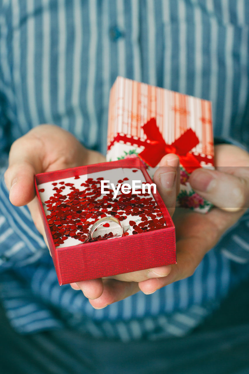 Midsection of man holding engagement ring box