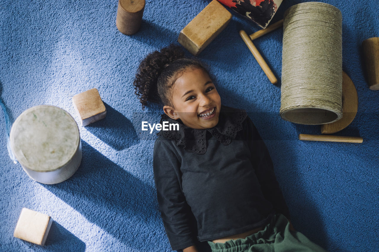 Portrait of smiling girl with toys lying on carpet at child care center