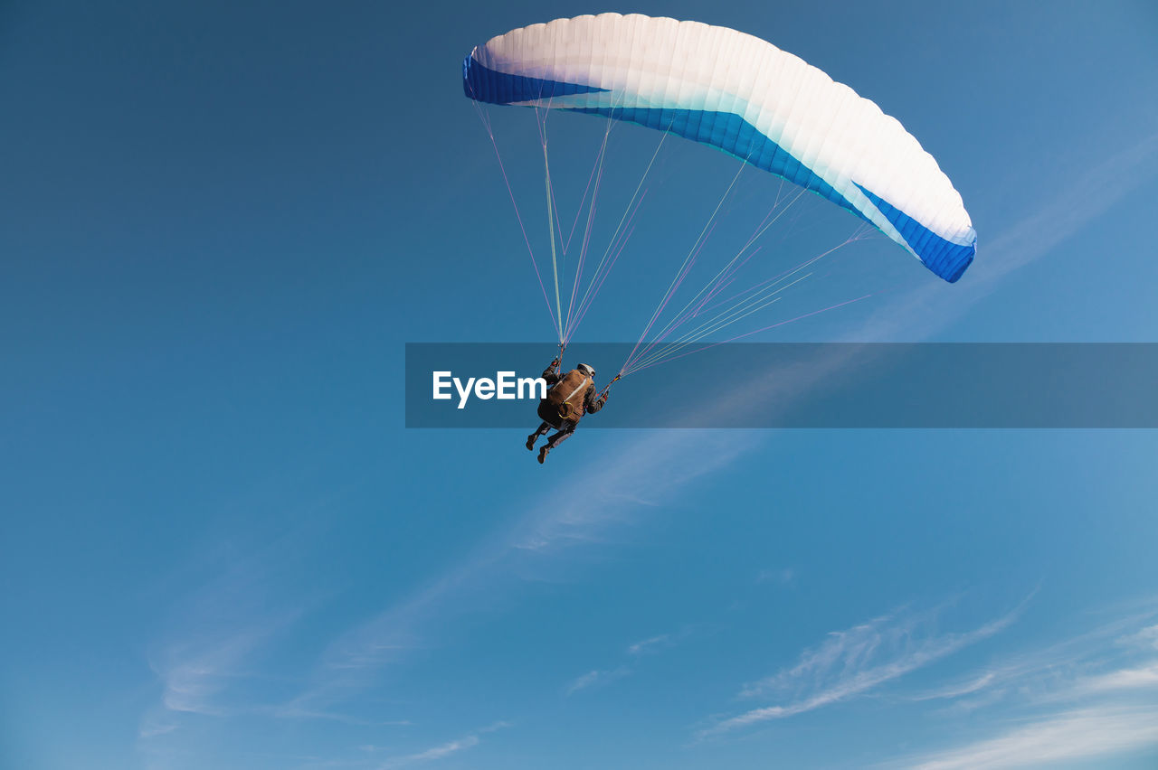 A paraglider takes off from a mountainside with a blue and white canopy and the sun behind. a