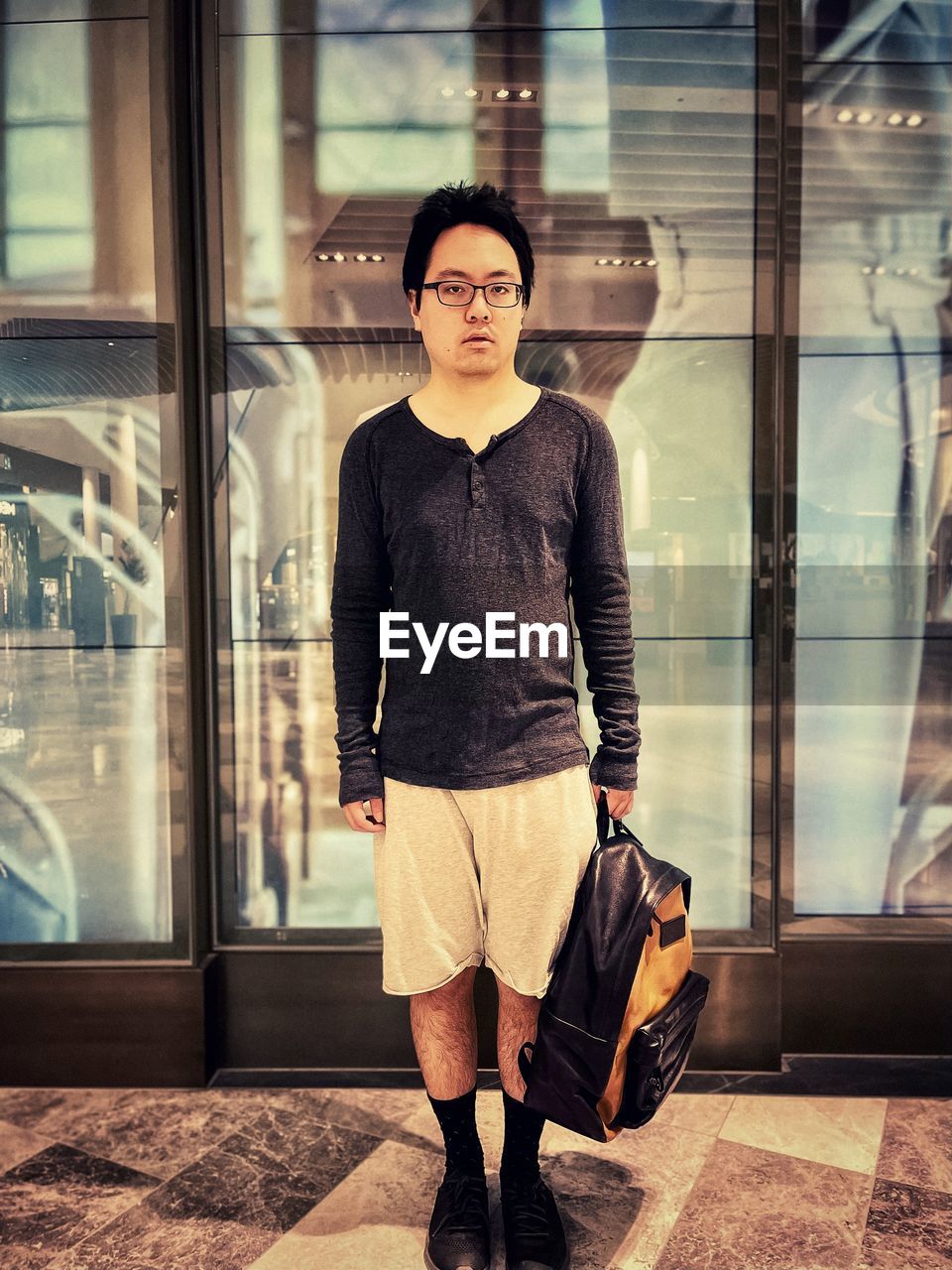 Portrait of young asian man in eyeglasses standing in front of illuminated reflective panels.