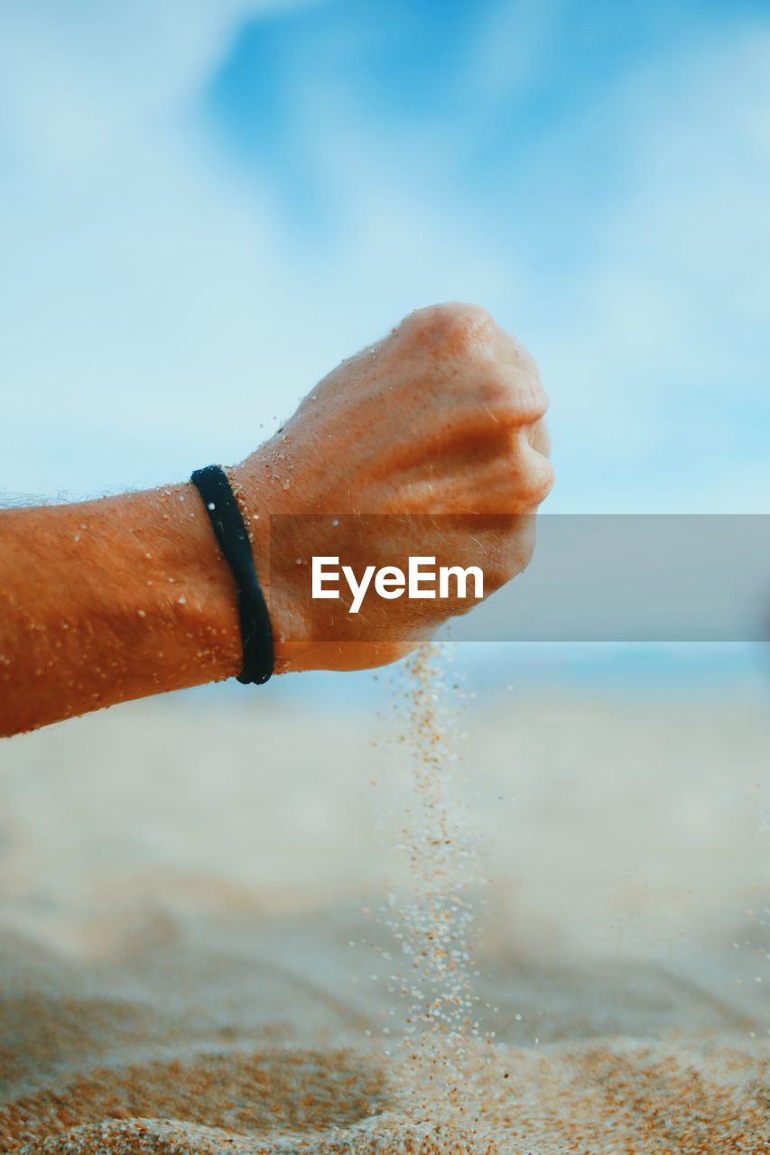 Cropped hand of man holding sand at beach