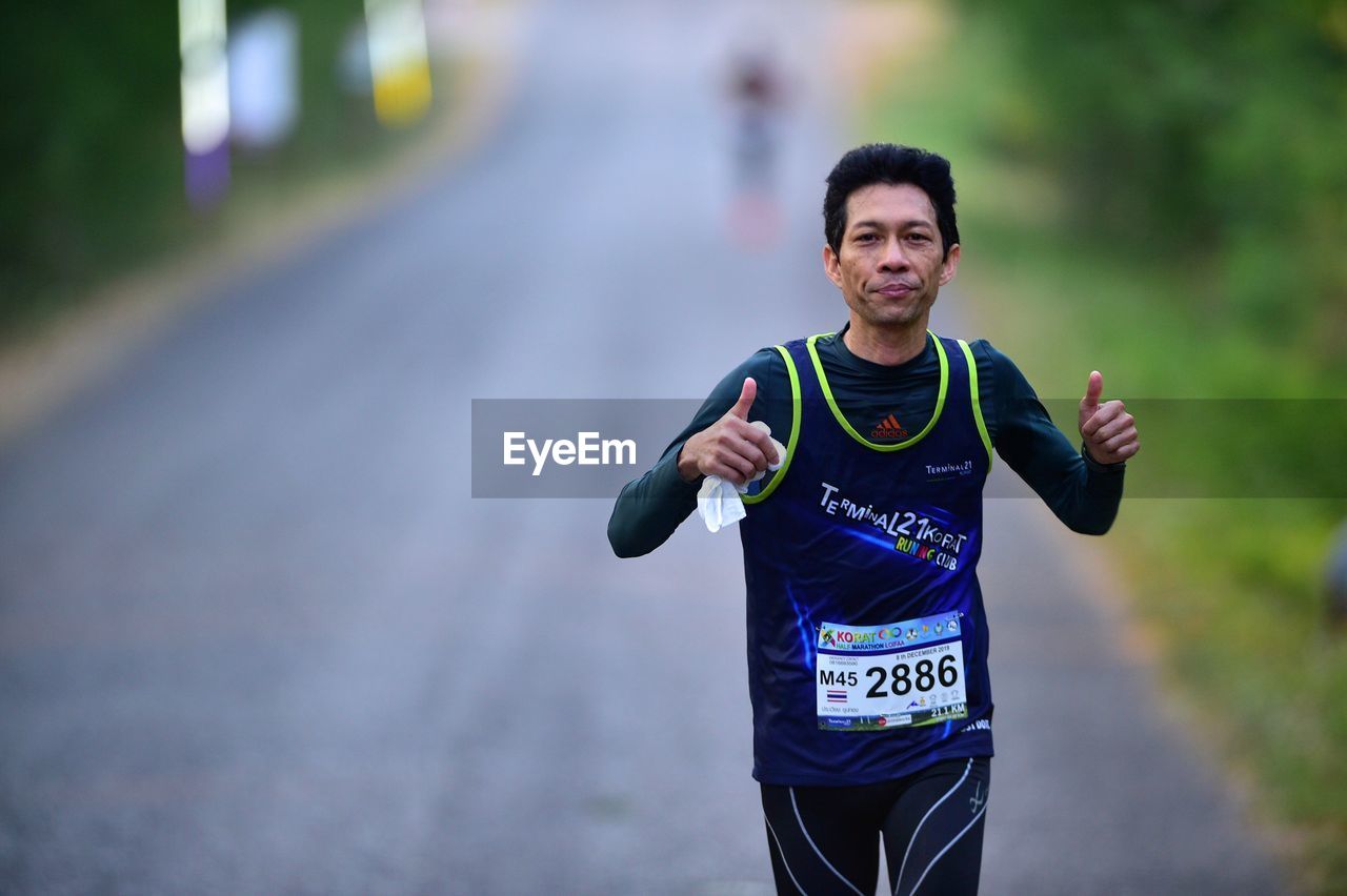 PORTRAIT OF YOUNG MAN RUNNING AGAINST BLURRED BACKGROUND