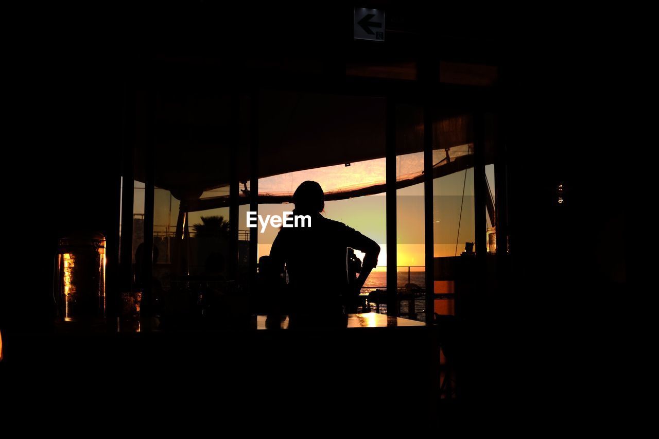 Silhouette person standing against window during sunset