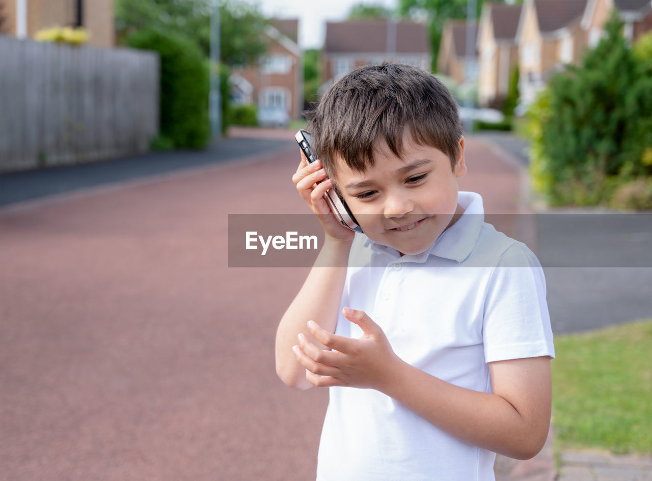 Portrait happy schoolboy talking on mobile phone with friend. cute child using smart phone 