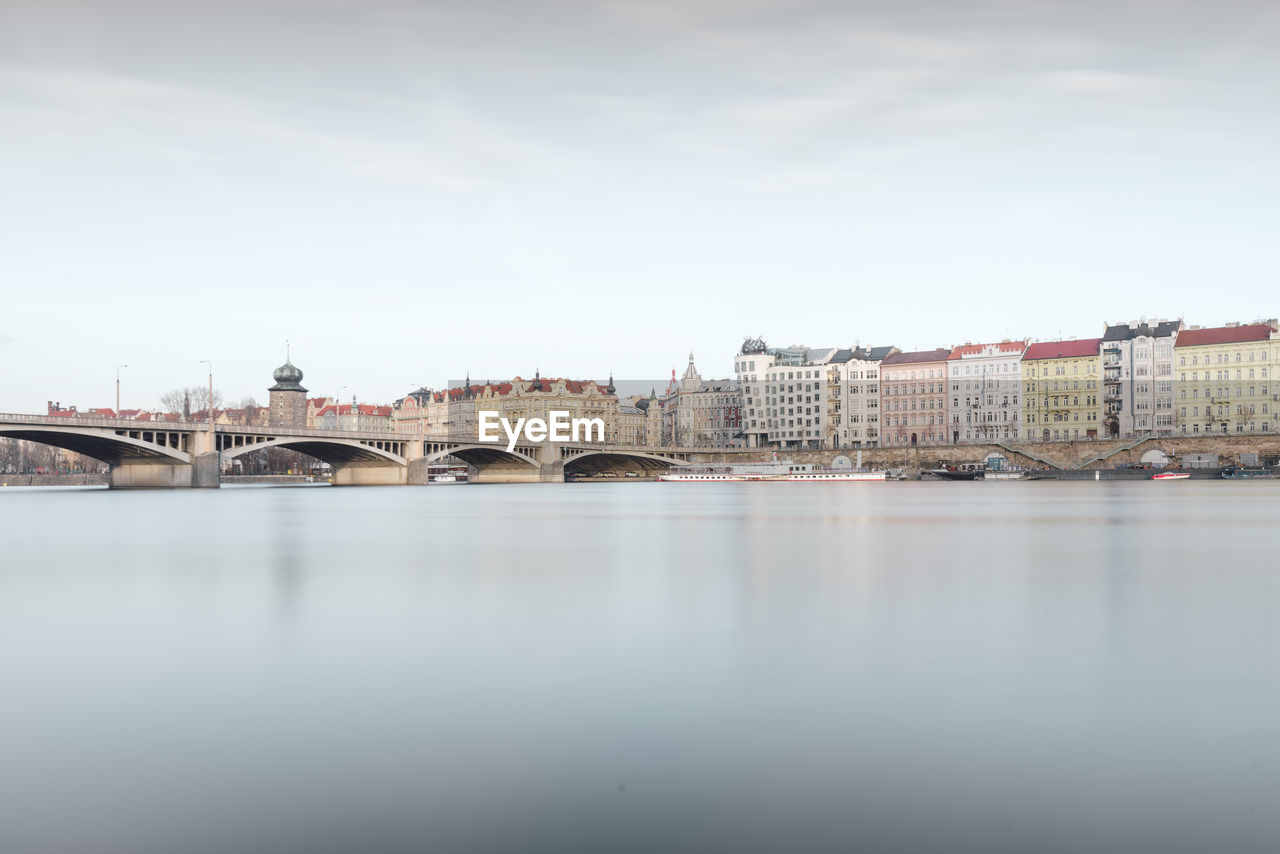 Bridge over river by buildings against sky in city