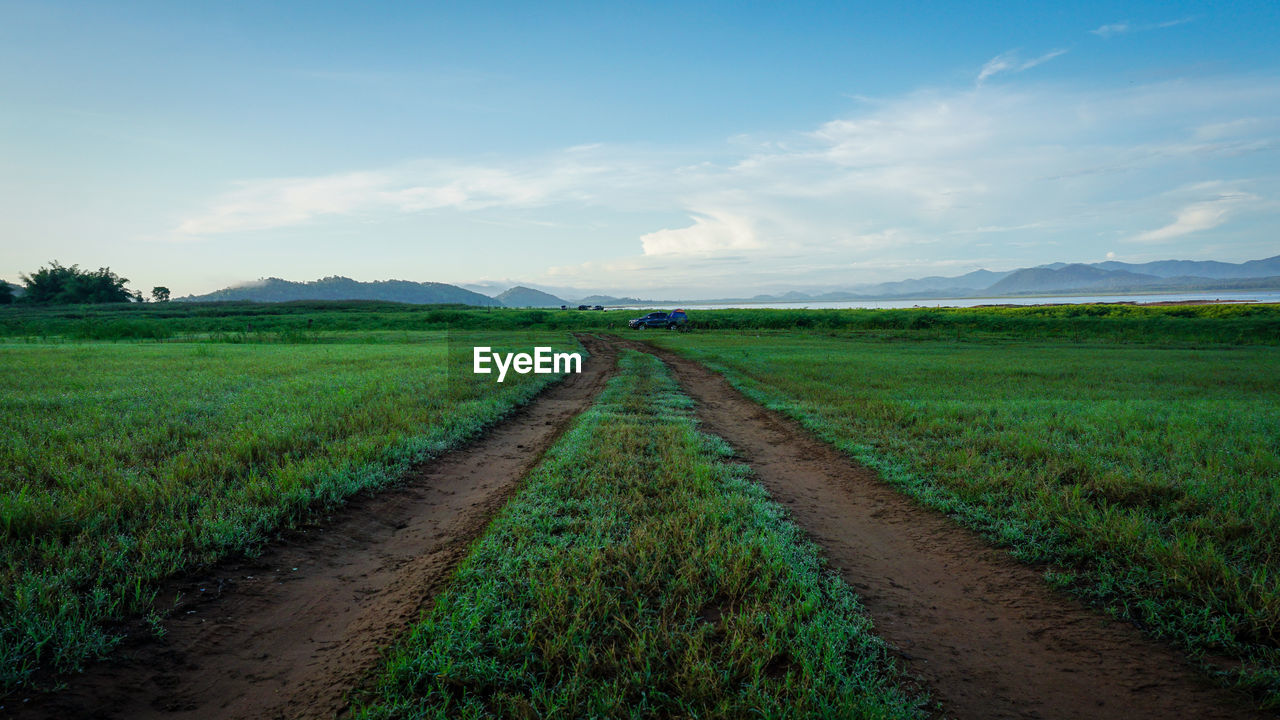 Dirt road amidst field against sky