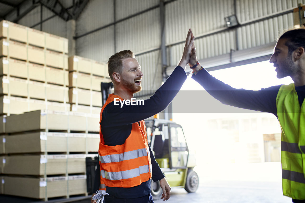 Happy colleagues in protective workwear high fiving in factory