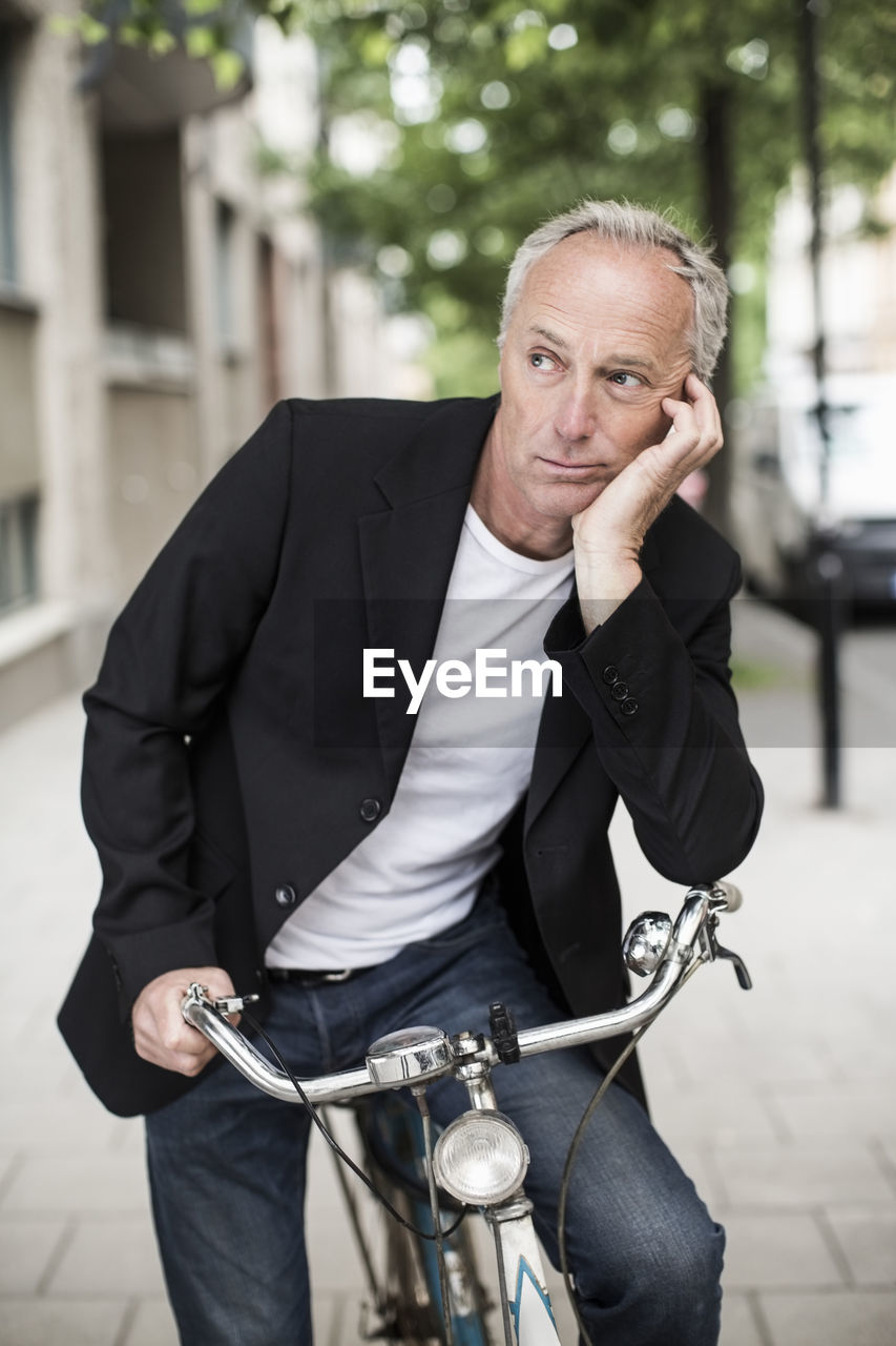 Thoughtful businessman looking away while sitting on bicycle at sidewalk