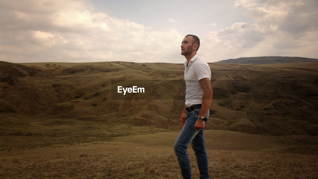 Side view of young man standing against sky on land