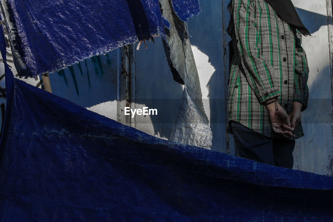 Midsection of woman standing by wall and tarpaulin