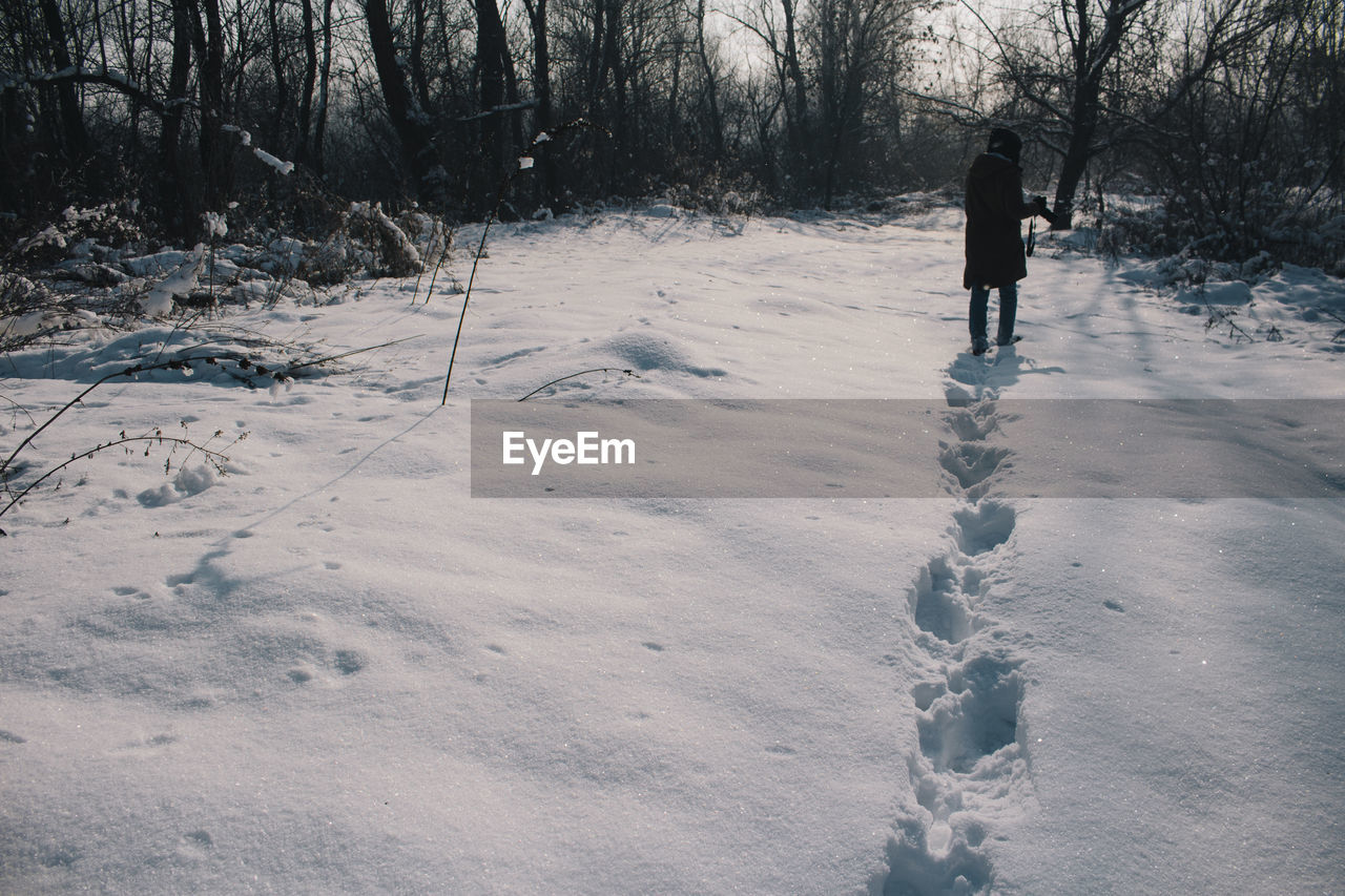 REAR VIEW OF MAN WALKING ON SNOW COVERED TREES