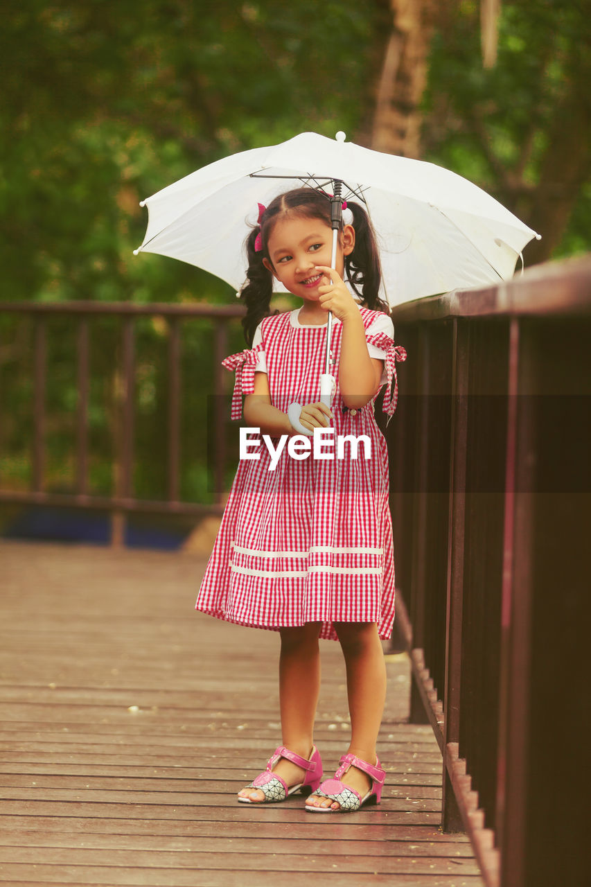 Full length of cute girl standing at railing while holding umbrella