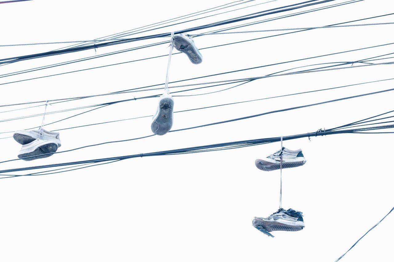 Low angle view of shoes hanging in power cables against clear sky