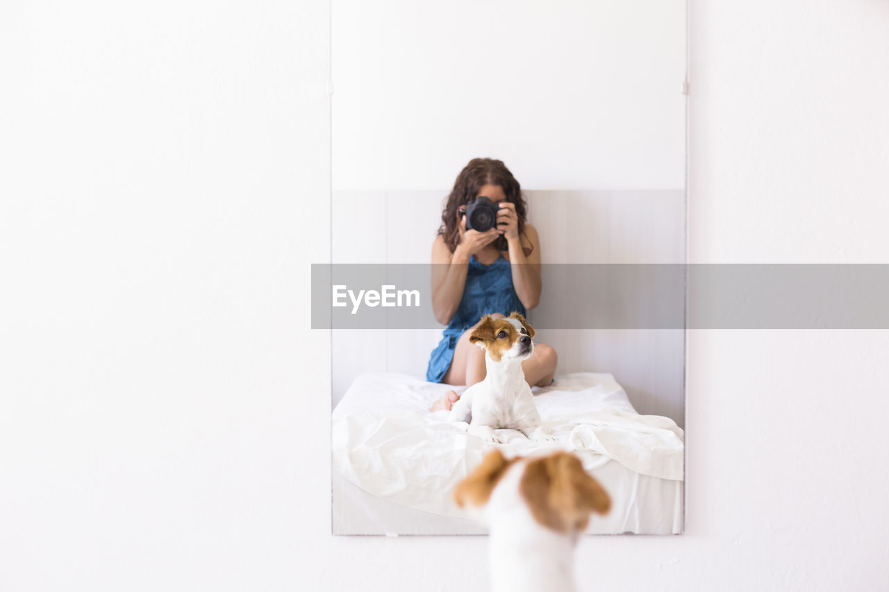 Reflection of woman photographing by dog in mirror at home