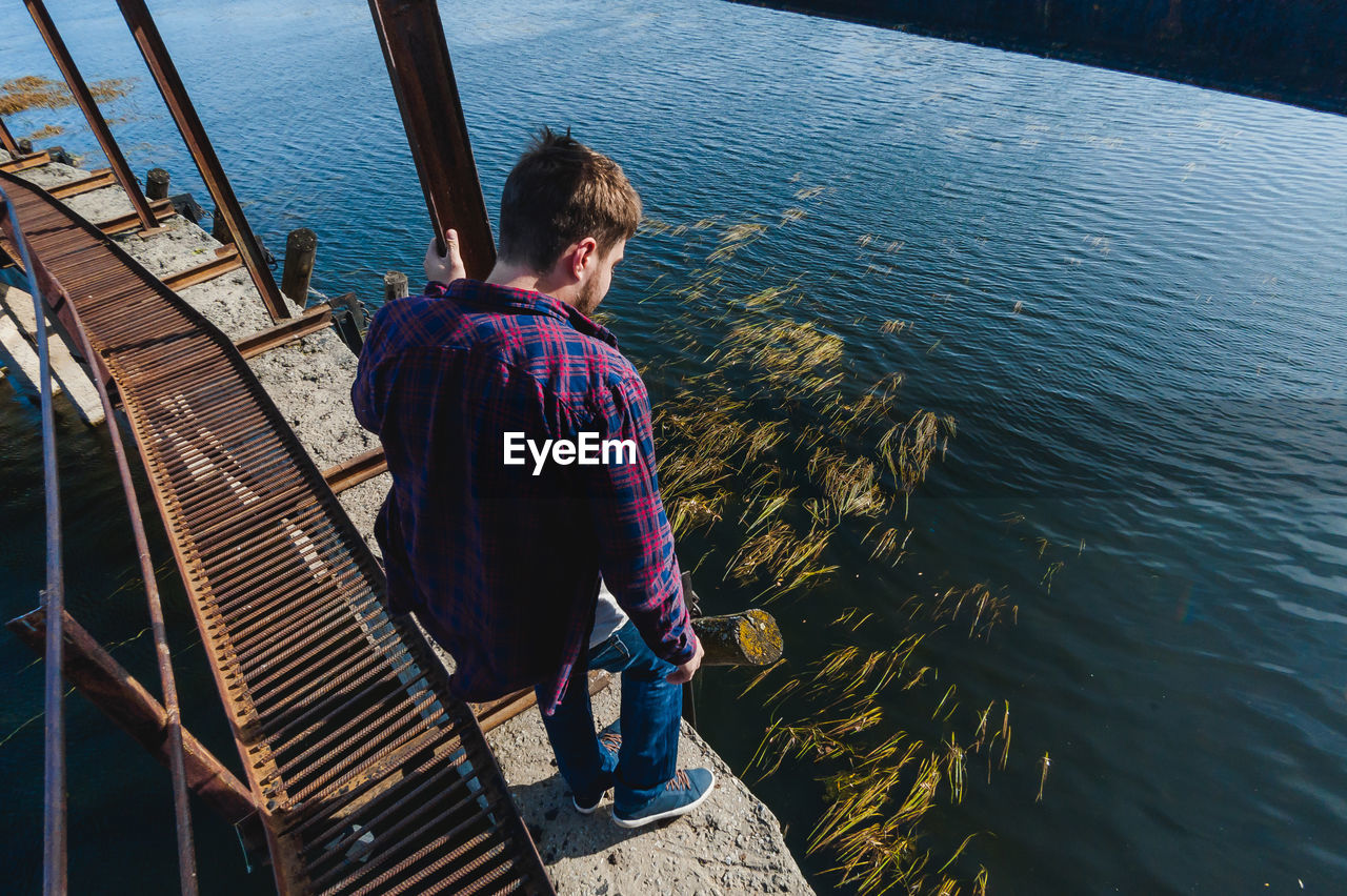 High angle view of man standing on retaining wall by river