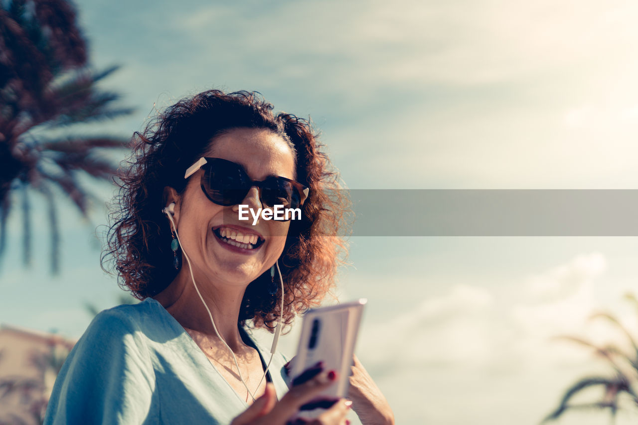 Portrait of happy woman using mobile phone against sky