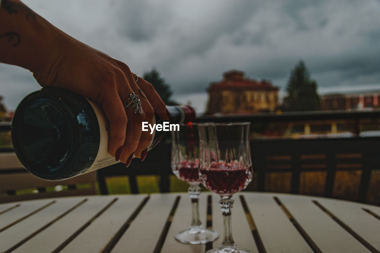 Hand holding wine glass on table against sky