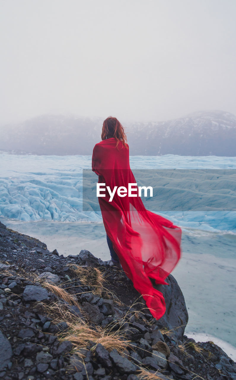 Elegant lady with red fabric on rock scenic photography