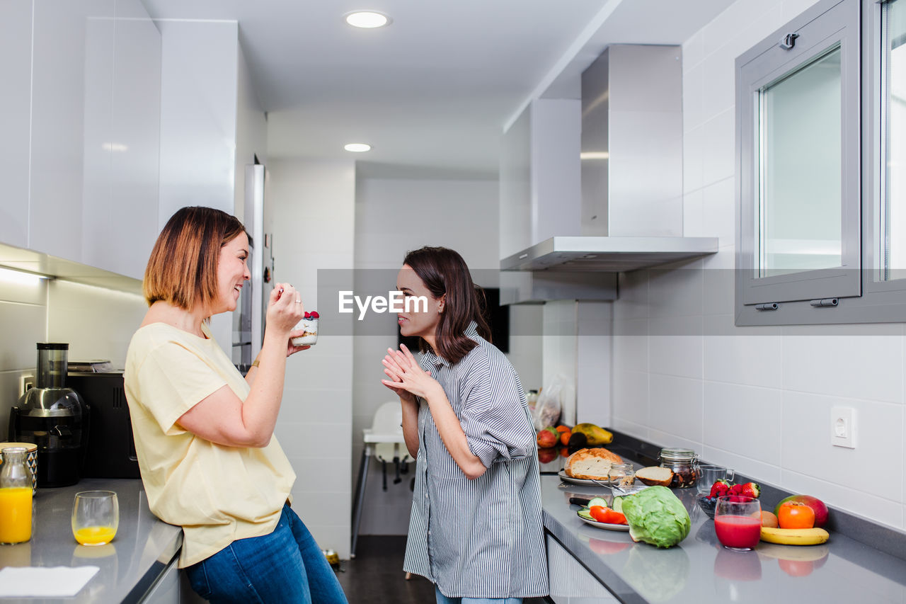 Cheerful women talking while standing in kitchen