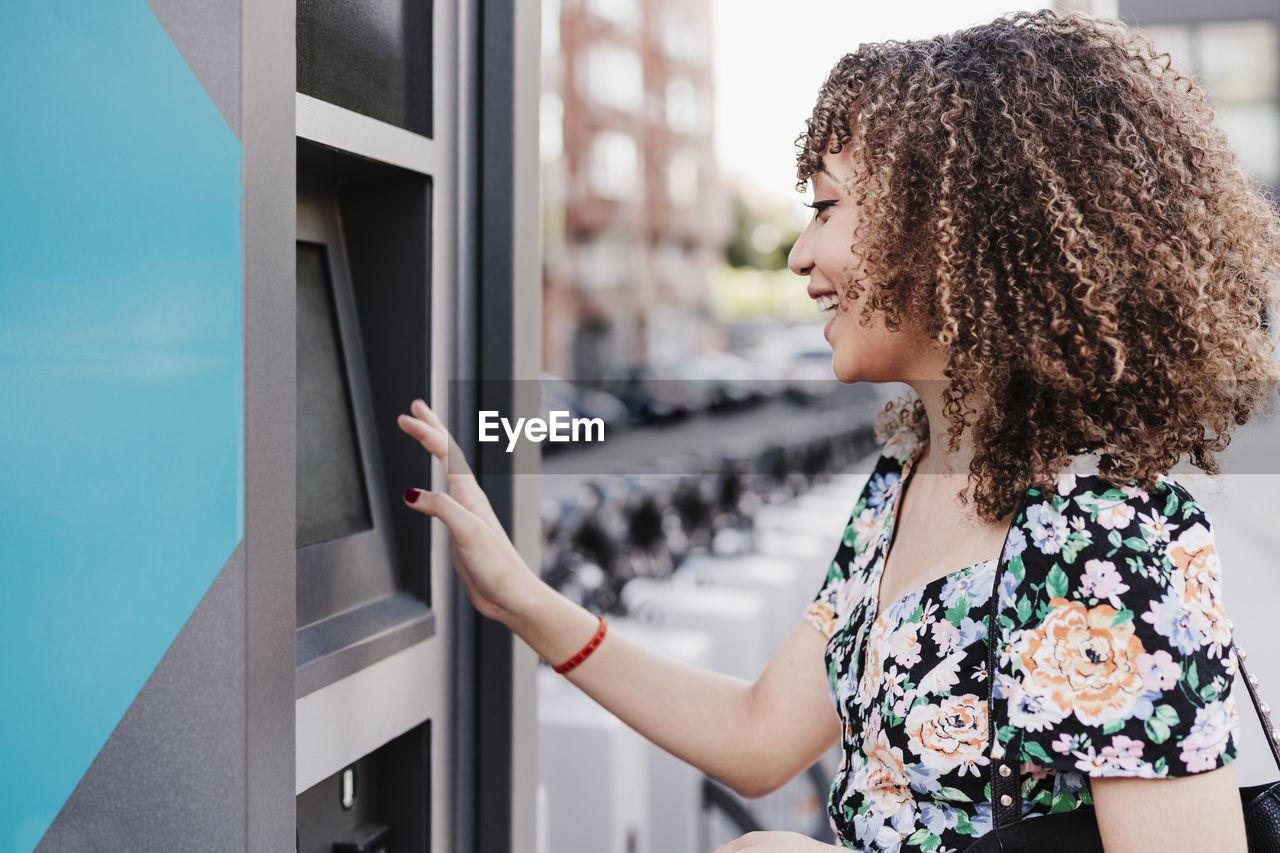 Cheerful young woman with curly hair payment machine for bicycle sharing system