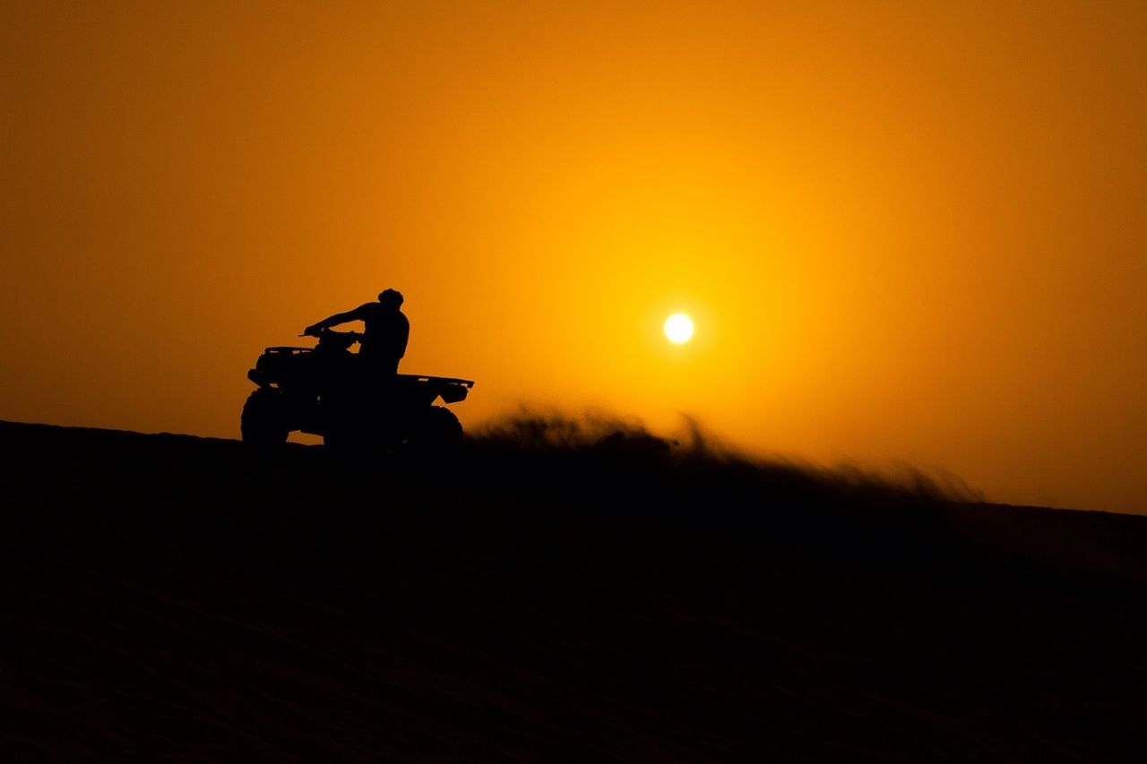 Silhouette of man driving quadbike at sunset