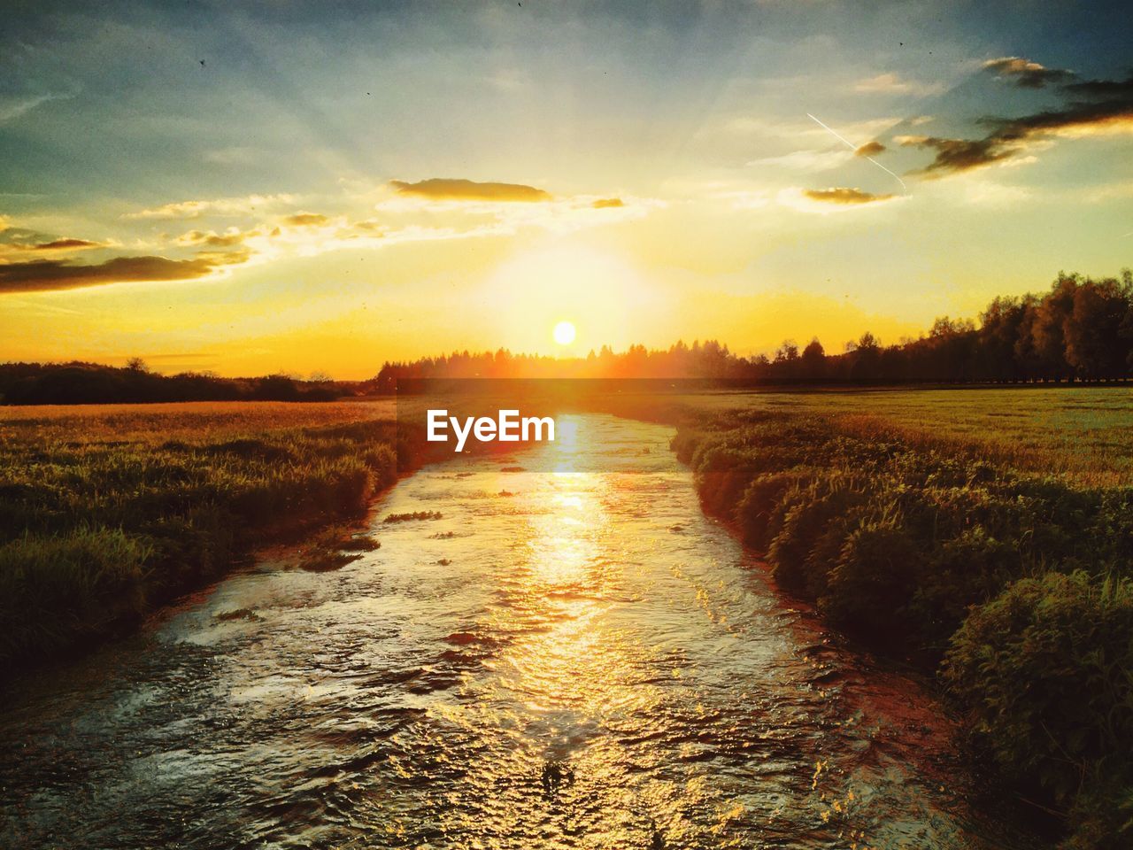 River amidst field against sky during sunset