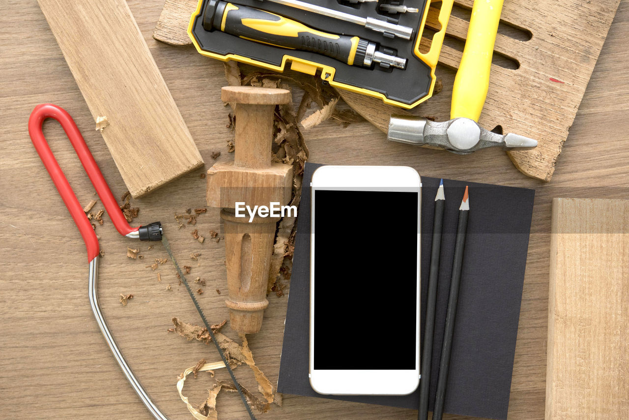 Directly above shot of mobile phone with wood and hand tools on table