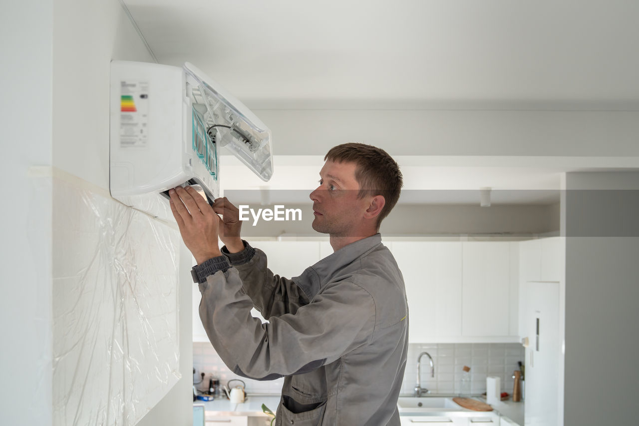 Man technician woker in uniform installing air conditioner in modern apartment.